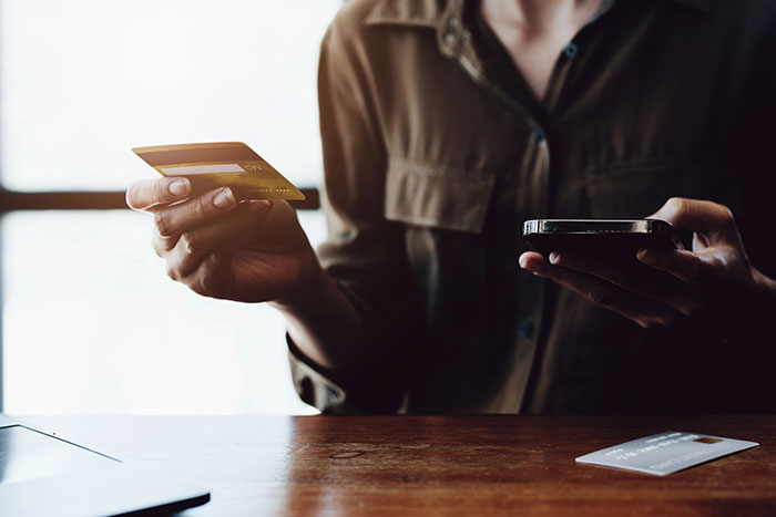 A woman holding a credit card in one hand and a smartphone in the other, engaged in an online transaction.