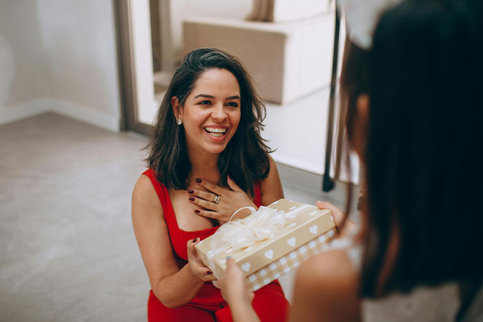 A child presents a wrapped gift to her smiling mother, celebrating Mother