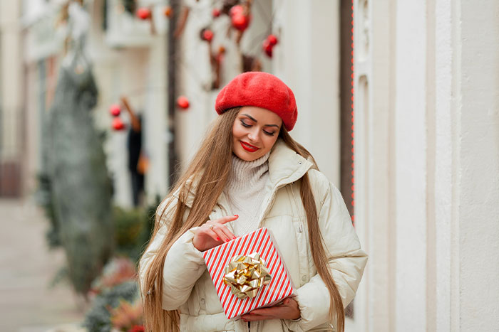Woman holding a wrapped gift box, wearing a red beret and white coat.