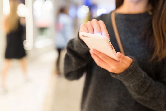 Person using a smartphone in a brightly lit indoor setting, wearing a dark sweater.