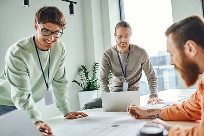Three people collaborating in a bright office setting with documents and a laptop.